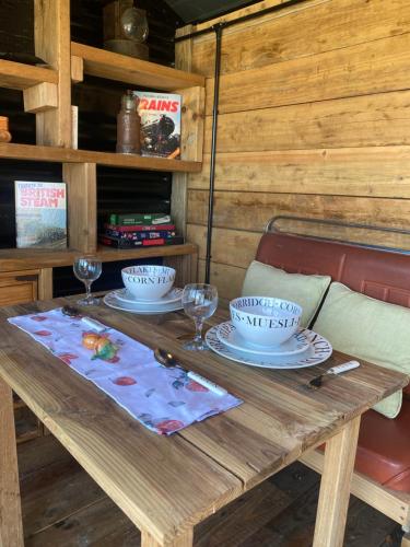 a wooden table with two plates and glasses on it at Swallowfield Glamping-Station Master in Yeovil