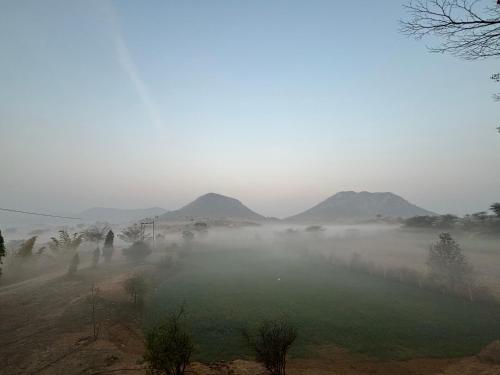 a field in the fog with mountains in the background at The Bainada farm in Jaipur