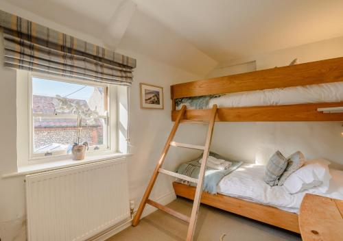 a bedroom with two bunk beds and a window at Parsley Cottage in Blakeney
