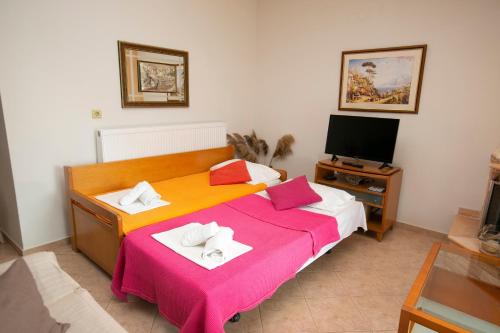 um quarto com uma cama com lençóis cor-de-rosa e uma televisão em House Stella em Keramoti