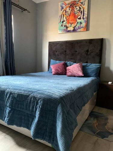 Schlafzimmer mit einem Bett mit blauer Bettwäsche und rosa Kissen in der Unterkunft Perchment view Apartment in Lusaka