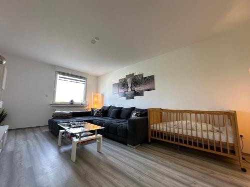 ein Wohnzimmer mit einem schwarzen Sofa und einem Kinderbett in der Unterkunft Zur schönen Aussicht I 90 m² I Idyllisch I Zuhause in Dortmund