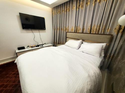 - une chambre avec un lit blanc et une télévision murale dans l'établissement Cozy Ghana Airport Studio at Kass Towers, à Accra