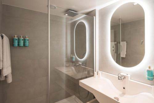 une salle de bain avec un lavabo et un miroir dans l'établissement Novotel Bordeaux Lac, à Bordeaux