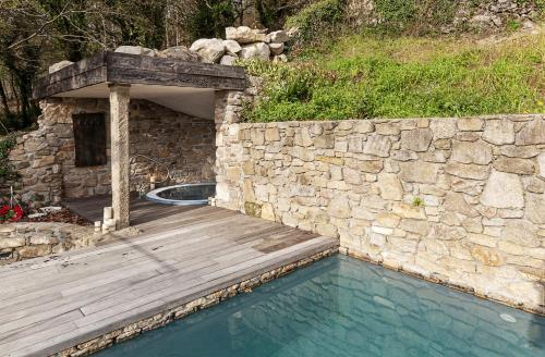 a swimming pool with a wooden deck next to a stone wall at Casa do Cebro Casa con piscina y jacuzzi privados in Santiago de Compostela