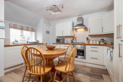 a kitchen with white cabinets and a wooden table and chairs at Stables Loft - Elie in Elie