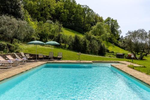 a swimming pool with chairs and umbrellas on a hill at Podere San Bartolo- Fienile in Barberino di Val dʼElsa