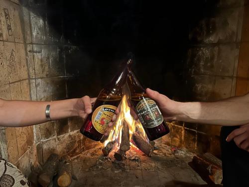 two people holding beer bottles over a fire at Hostel Otto Tipp in El Bolsón