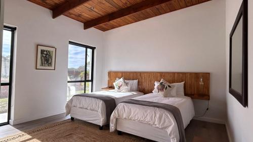 two beds in a room with white walls and windows at Kiepersol in Gansbaai