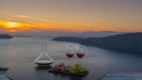 two glasses of wine sitting on a table with grapes at Arany Terra in Imerovigli