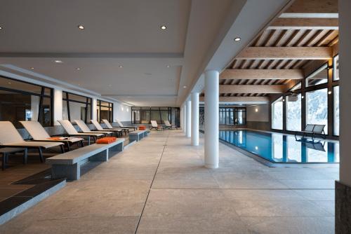 a swimming pool in a building with tables and chairs at Hôtel Alpen Lodge in La Rosière