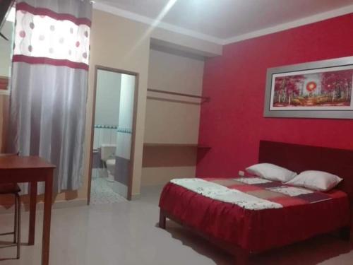 a bedroom with a red wall with a bed and a desk at Hostal Los Angeles in Tarapoto