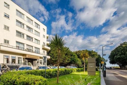 a building with a palm tree next to a street at Queens Hotel & Spa Bournemouth in Bournemouth