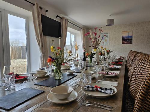 a long wooden table with flowers and plates on it at The Plough Inn Farmhouse - Private Holiday House in Lenwade