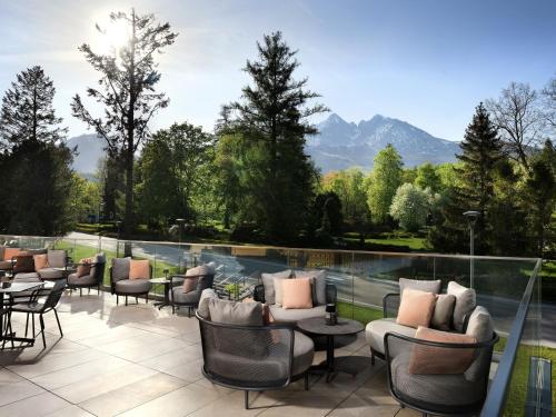 un patio con sillas, mesas y montañas de fondo en Hotel Lomnica en Tatranská Lomnica