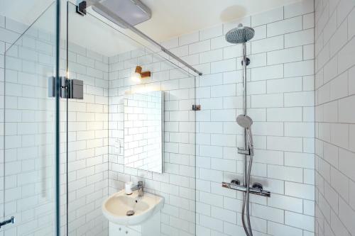 a white tiled bathroom with a shower and a sink at Domki Kuter Port in Gdów