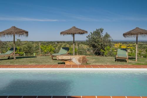 a swimming pool with two chairs and umbrellas at Alandroal Nature & Pool Retreat in Alandroal