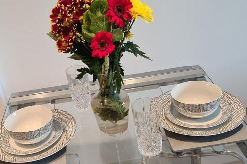 a glass table with plates and a vase with flowers at Guest Homes - Bakers Quay Apartment in Gloucester