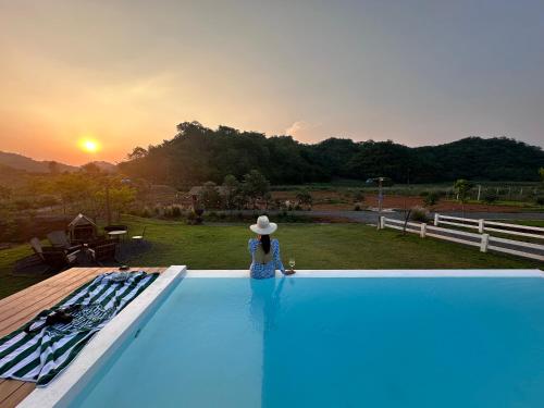 a woman sitting on the edge of a swimming pool at Maryland Khaoyai Annapolis Pool Villa in Ban Nong Song Hong