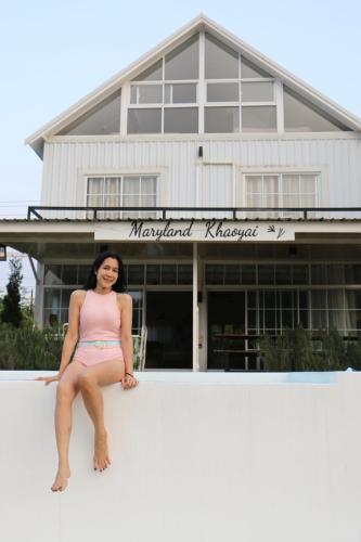 a woman sitting on a wall in front of a building at Maryland Khaoyai Annapolis Pool Villa in Ban Nong Song Hong
