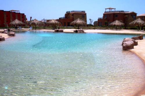 a swimming pool with blue water and straw umbrellas at jenlyn chalet-families only in Ain Sokhna