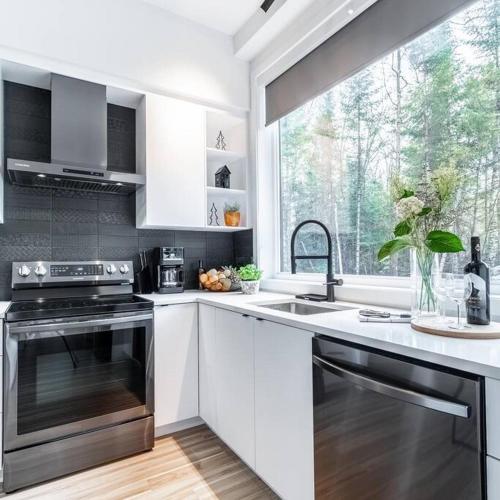 a kitchen with white cabinets and a sink and a window at Chalet Vintersaga Mont Tremblant in La Conception