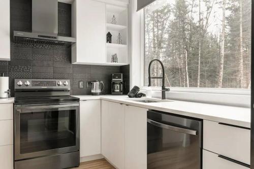 a kitchen with white cabinets and a sink and a window at Chalet Vintersaga Mont Tremblant in La Conception