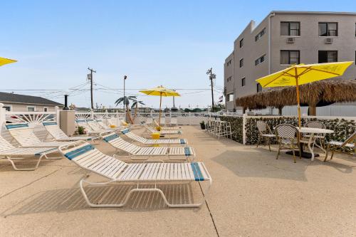 懷爾德伍德的住宿－Oceanic Hotel & Barefoot Tiki Bar，海滩上的一排躺椅和遮阳伞
