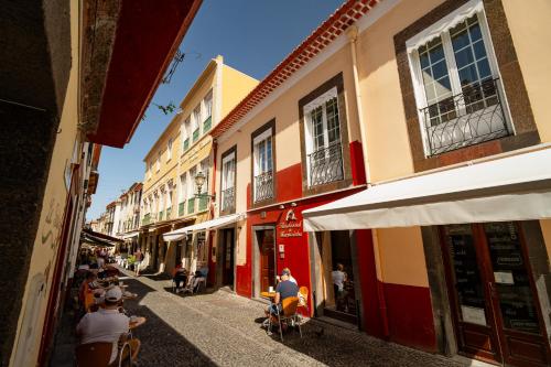 a group of people sitting on a street with buildings at O Cantinho da Mariazinha in Funchal
