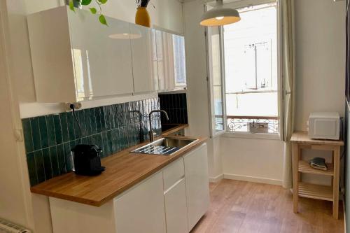 une cuisine avec des armoires blanches, un évier et une fenêtre dans l'établissement Nice appt close to Notre-Dame de la Garde, à Marseille