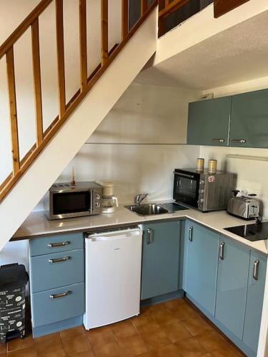 La cuisine est équipée de placards bleus et d'un réfrigérateur blanc. dans l'établissement Cocon Familial, à Saint-Raphaël