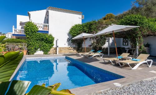 a swimming pool with chairs and umbrellas next to a house at Campo Agave B&B in Sayalonga