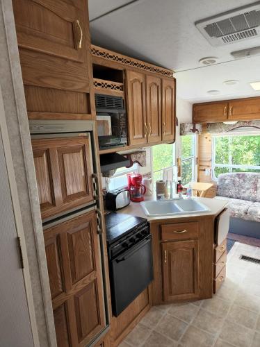 a kitchen with wooden cabinets and a sink in a caravan at Camping Beaurivage 1- Pret à camper entièrement équipée pour 6 personnes in Routhierville