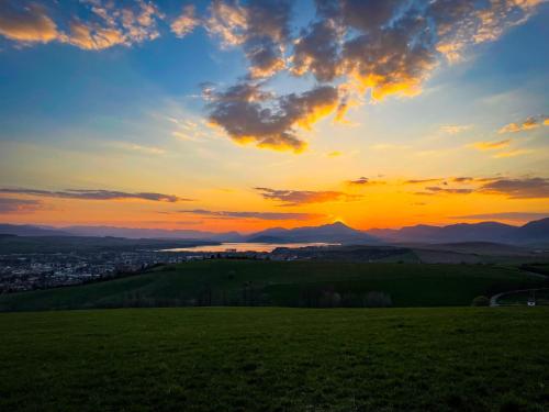 a sunset over a green field with a city at Chaty pri Mare - Tatralake Houses near Auqapark Tatralandia and Lake Liptovska Mara in Liptovský Trnovec