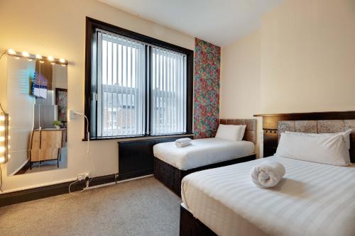 Una habitación de hotel con dos camas y una ventana. en Newcastle CITY APT5,FREE STREET PARKING,4 BEDROOM HOUSE WITH 2 FULL BATHROOM AND KITCHEN,ALL ROOMS WITH TVs,7 BEDS,NETFLIX, en Newcastle