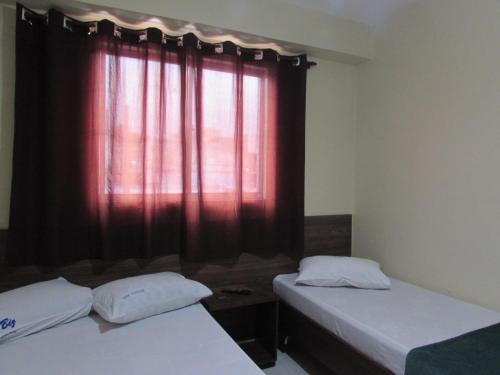 two beds in a room with a window with red curtains at Hotel Biz a 8 minutos do Brás, a 15 minutos da 25 de março e a 8 minutos do Bom retiro in Sao Paulo