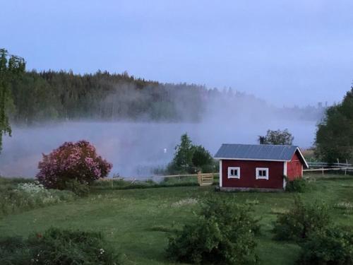 a small red house in a field with fog in the background at Country house Ruohoranta in Kuopio