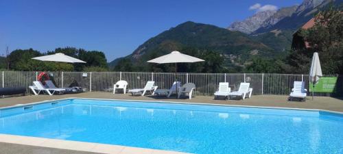 a swimming pool with chairs and umbrellas with mountains at Cosy du Birdie Logement 4 pers avec piscine in Giez