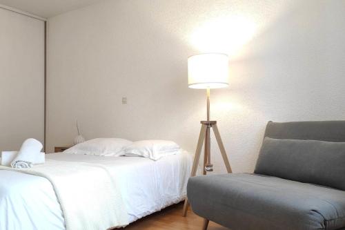 a bedroom with a bed with a lamp and a chair at Cosy du Birdie Logement 4 pers avec piscine in Giez