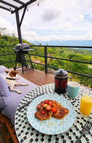 a table with a plate of food on a balcony with a dog at Manoah: cabaña en las montañas 2 in La Mesa
