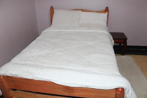 a bed with white sheets and a wooden headboard at Chaka Furnished Apartments in Kiganjo