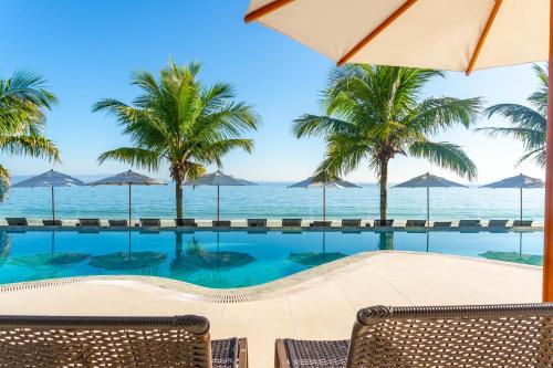 a pool with chairs and umbrellas and the ocean at Palace Praia Hotel in Florianópolis