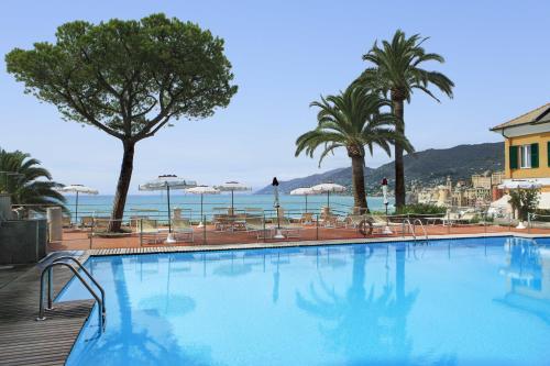 a large swimming pool with palm trees and the ocean at Hotel Cenobio Dei Dogi in Camogli