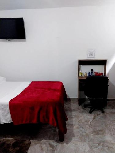 a bedroom with a bed with a red blanket and a desk at habitación cómoda en familia in Ibagué