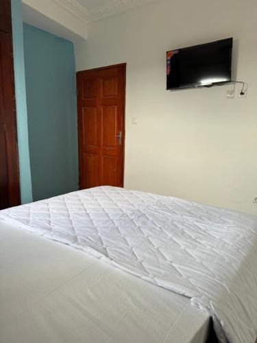 a bedroom with a white bed with a television on the wall at Lekker Estate in Yaoundé