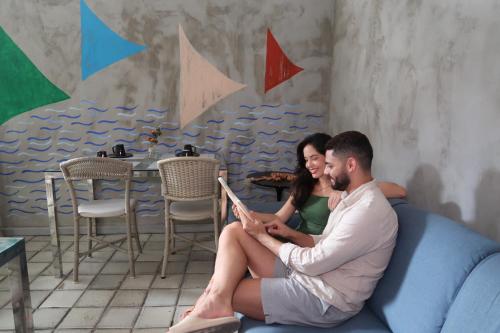 un hombre y una mujer sentados en un sofá leyendo un libro en Pousada Praia Pajuçara, en Maceió