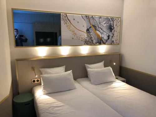 uma cama com lençóis brancos e um espelho por cima em Brit Hotel Orléans St Jean de Braye - L'Antarès em Saint-Jean-de-Braye