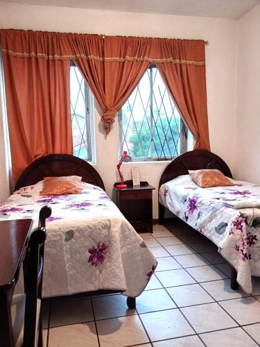 two beds in a room with two windows at Hostal Almagro in Quito