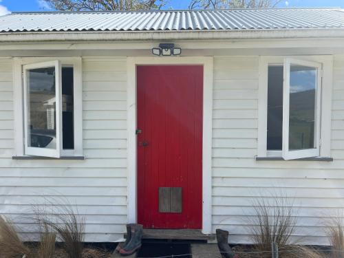 una porta rossa su una casa bianca con due finestre di Pohokura Farmstay a Taihape