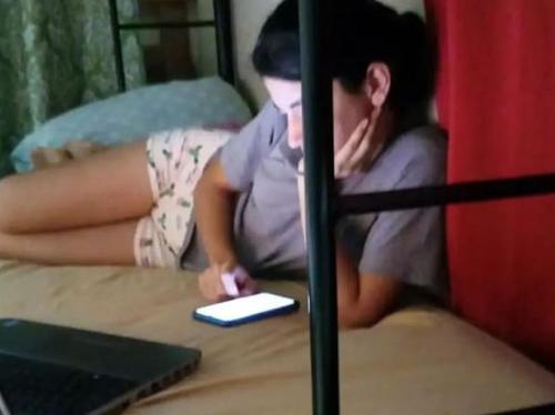 una mujer sentada en una cama mirando un celular en Puruha Inn, en Riobamba